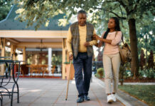 Smiling woman walking with her senior father while visiting him at nursing home.