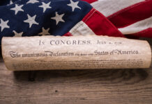 United States Declaration of Independence rolled in a scroll on a vintage American flag and rustic wooden board